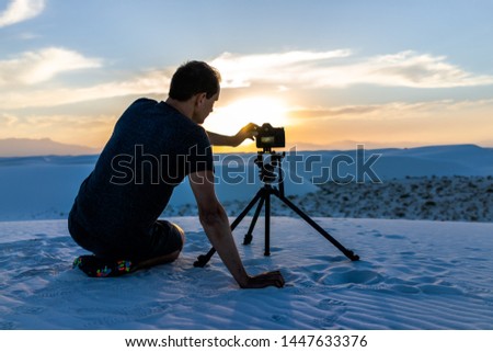 Man photographer with tripod sitting with camera in white sands dunes national monument in New Mexico view of sunset