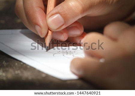 Closeup childs hand draws a flower with a pencil on a white sheet of paper, selective focus