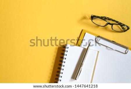 Yellow color office table top view with clipboards with paper, reading glasses, memo pad and pen. Copy space
