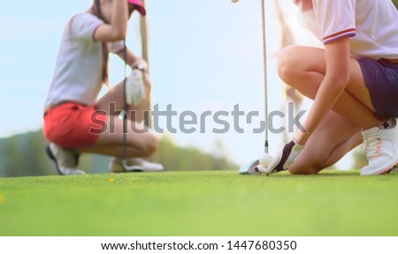 hand of young woman golf player holding golf ball laying on wooden tee, prepare and ready to hit the ball to the destination target, opponent competitor or golf mate buddy watching in background