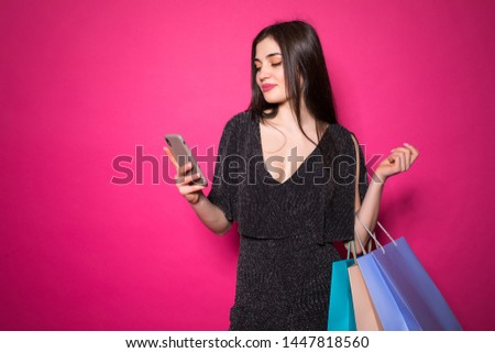 Image of a woman posing holding shopping bags using mobile phone isolated over pink background