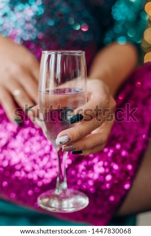 woman in a glittery red dress with a glass of champagne toast sits in a green chair