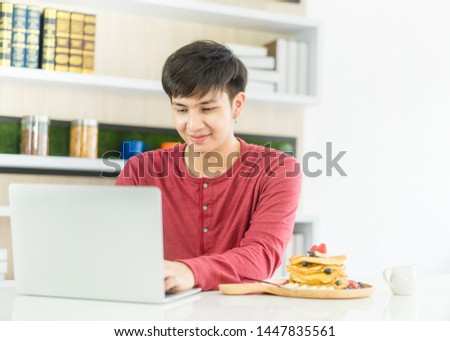 University student man typing work laptop in kitchen table at campus room in the morning.Asian man work at home.