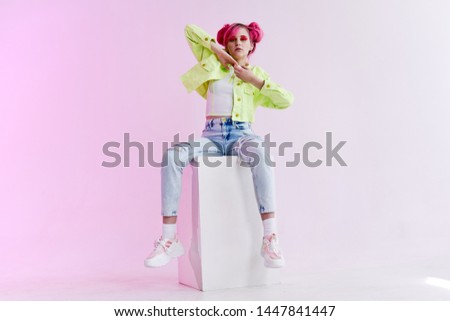 young woman with hairstyle in stylish clothes sits on a cube 