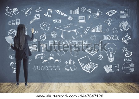 Back view of young businesswoman drawing business sketch on wall of chalkboard interior. Education and knowledge concept 