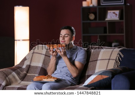 Handsome young man eating unhealthy food while watching TV at night