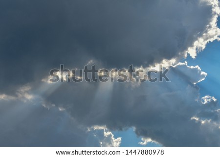 The sun's rays make their way through the dark clouds. Blue sky surrounded by gray clouds.