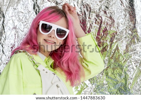 woman in glasses with pink hair smiling foil background