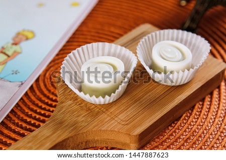 Handmade white chocolate candies on a wooden board next to a book and a picture