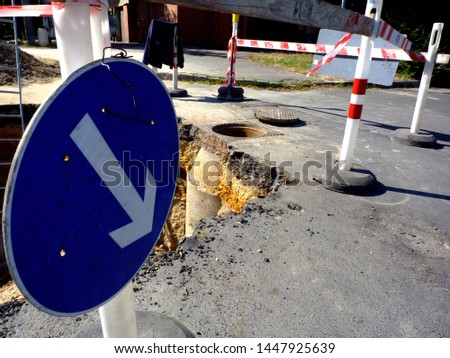 large excavation after road collapse of asphalt surface. the result of erosion caused by storm water. road works. under repair & construction. road hazard. red & white wood safety barrier traffic sign