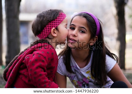 A beautiful child, a girl gets a kiss from her younger sister. Portrait outdoors in the park. Blurred background.