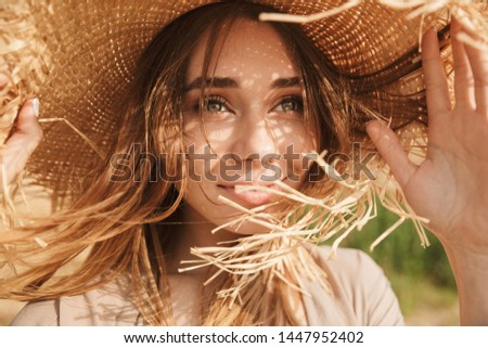 Portrait of young optimistic smiling gorgeous beautiful woman posing outdoors at the sea beach wearing hat.