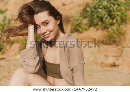 Photo of a gorgeous smiling young woman in swimwear posing outdoors at the beach sea.