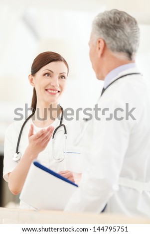 Consulting with a colleague. Young female doctor standing in front of her mature colleague gesturing and smiling