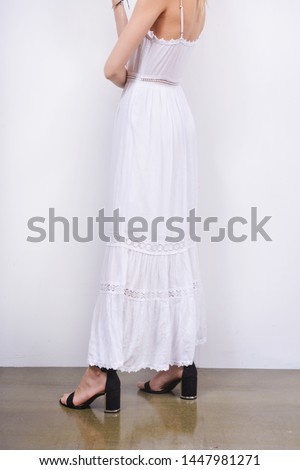 women in fashion white long dress with black shoes posing on gray background
