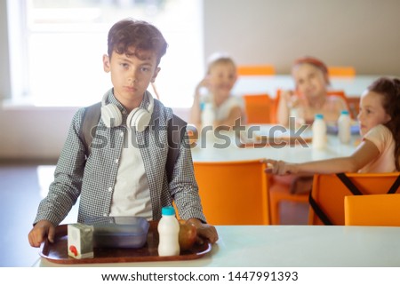 Feeling like outcast. Dark-haired boy holding tray with food feeling like outcast while eating alone in canteen Royalty-Free Stock Photo #1447991393
