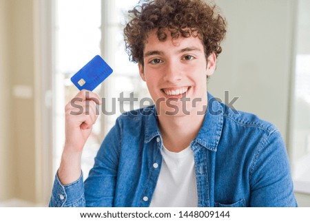 Young man holding credit card with a happy face standing and smiling with a confident smile showing teeth