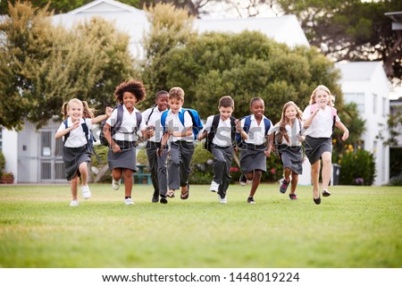 Excited Elementary School Pupils Wearing Uniform Running Across Field At Break Time Royalty-Free Stock Photo #1448019224