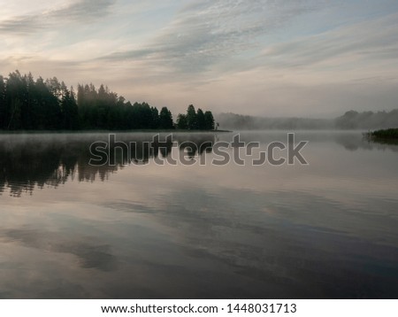 Foggy and mystical lake landscape before sunrise. All silhouettes are blurry and unclear. Vaidavas lake, Latvia