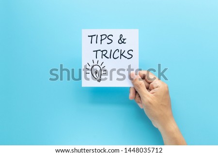 text tips and tricks on white paper in hand isolated on blue background
