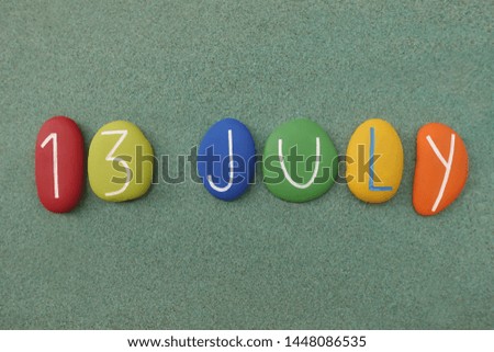 13 July, calendar date composed with multi colored stones over green sand