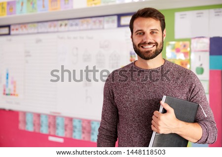 Portrait Of Male Elementary School Teacher Standing In Classroom Royalty-Free Stock Photo #1448118503