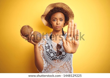 Young african american woman with afro hair holding coconut over yellow isolated background with open hand doing stop sign with serious and confident expression, defense gesture