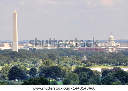 Elevated, panoramic view of the National Mall in Washington DC. The Washington Monument to the left and the United States Capitol building on the right.  Green tree tops of summer in the foreground.
