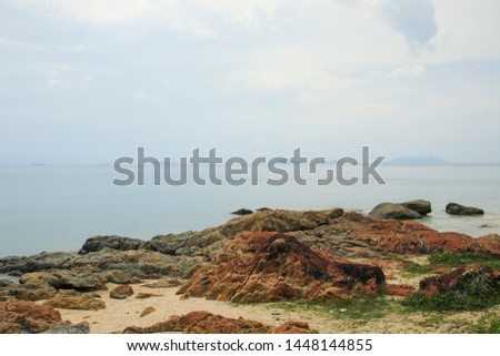 Landscape of a calm afternoon by the sandy beach with rocks under blue sky with clouds, islands seen on the horizon in the background, selective focus