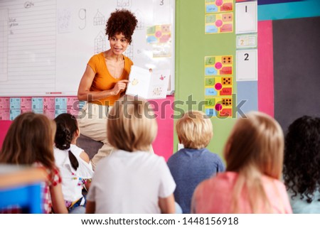 Female Teacher Reading Story To Group Of Elementary Pupils In School Classroom Royalty-Free Stock Photo #1448156918