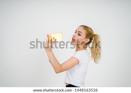 Blonde girl with ponytails taking happy selfie smiling with yellow smartphone