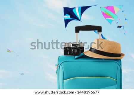 recreation image of traveler luggage, camera and fedora hat infront of blue sty with flying colorful kites background. holiday and vacation concept