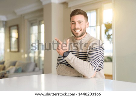 Young handsome man at home cheerful with a smile of face pointing with hand and finger up to the side with happy and natural expression on face