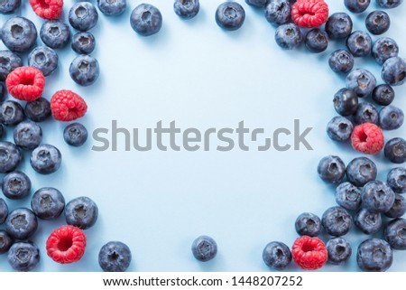 Frame made of blueberries and rapberries on blue background, view from above, free space