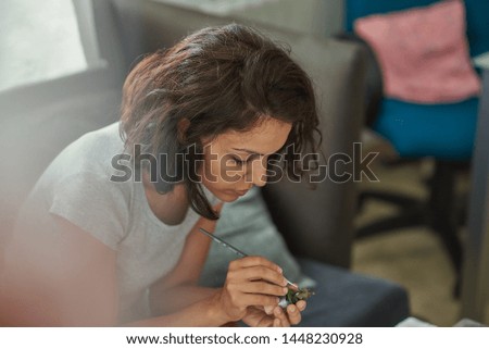
Brunette woman of latin race painting small figures with a white background.