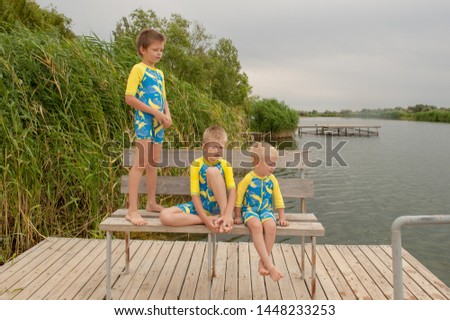 Funny kids in bathing suits sit together on wooden bridge near river. boys are happy on vacation in village together. Summer day, river, swimming in the water