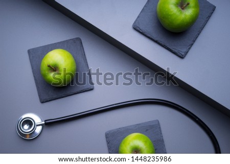 An apple a day keeps the doctor away concept. Stethoscope and green apple concept for diet, healthcare, nutrition or medical insurance on grey based background. Flat lay or top view.