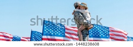 panoramic shot of military man holding in arms cheerful child near american flags 