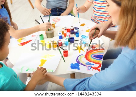 Female teacher with children at painting lesson indoors