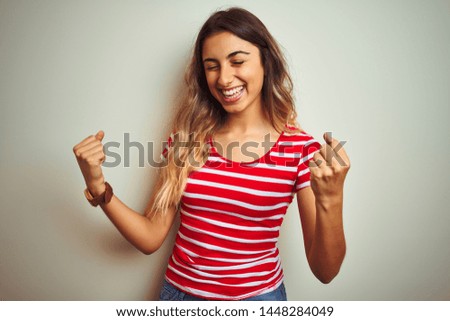 Young beautiful woman wearing red stripes t-shirt over white isolated background very happy and excited doing winner gesture with arms raised, smiling and screaming for success. Celebration concept.
