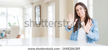 Wide angle picture of beautiful young woman sitting on white table at home afraid and terrified with fear expression stop gesture with hands, shouting in shock. Panic concept.