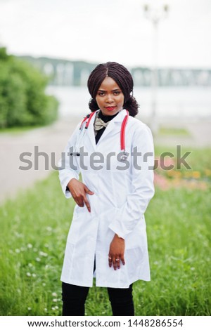 Young african american female doctor in white coat with a stethoscope posed outdoor.
