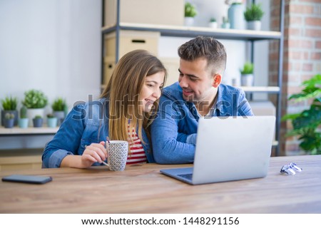 Young couple relaxing drinking a coffee and using the computer laptop around cardboard boxes, very happy moving to a new house