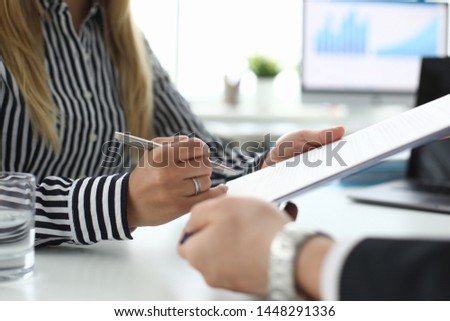 Focus on tender female hand signing corporate contract. Woman in trendy clothes holding distinctive document and sitting in modern biz office with partner. Blurred background