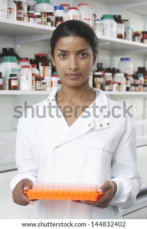 Portrait of female pharmacist holding tray of test tubes in pharmacy