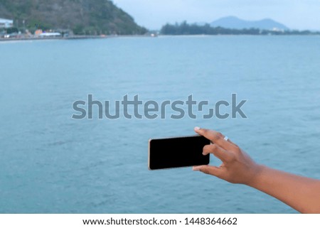 The mobile phone black screen at hand with sea blurred background, The image use for selfie with friend group