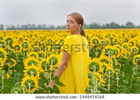 Young woman in yellow dress in summer sunflower field
