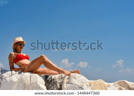 Beautiful girl in red bikini sitting on a rock by the sea.