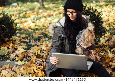 Young blogger woman with dog, laptop, and cup of latte in autumn park