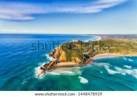 Byron Bay lighthouse high on the rocky headland - the most eastern point of Australian continent facing Pacific ocean in elevated aerial seascape above coast. Royalty-Free Stock Photo #1448478929